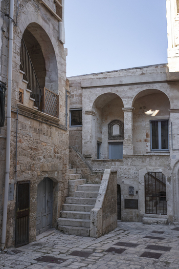 View of historic stone buildings with arched doorways and an outdoor staircase in a narrow courtyard Polignano a Mare Apulia Italy.
