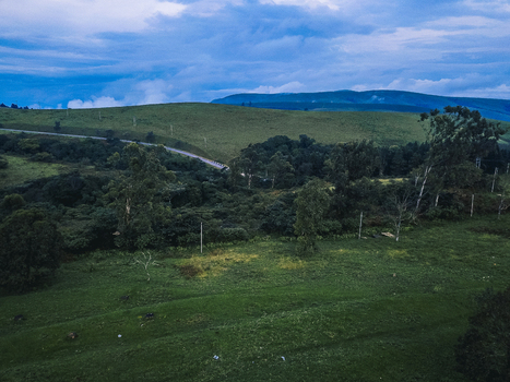 Aerial view of sweeping verdant hills under a dramatic moody sky with a winding road cutting through the lush landscape Obudu Cross River Nigeria.