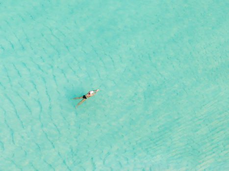 Aerial view of a lone swimmer adrift in the turquoise waters near Kan island Dhidhdhoo Thiladhunmathi Atoll Maldives.