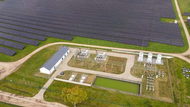 Aerial view of a large solar farm featuring rows of photovoltaic panels a central electrical substation with transformers a small utility building and a green water basin Poland.