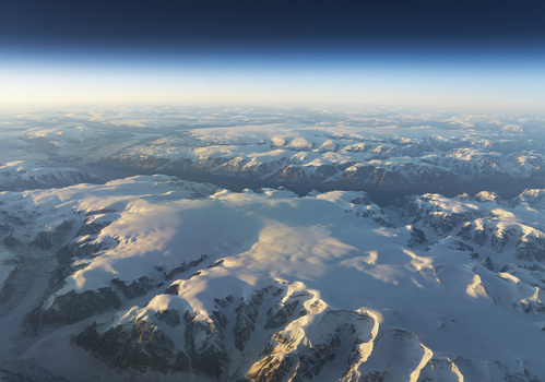Aerial view of the vast snow covered mountain ranges and massive glacial ice sheets under a clear blue sky during golden hour Greenland. Aerial view of the vast snow covered mountain ranges and massive glacial ice sheets under a clear blue sky during golden hour Greenland.
