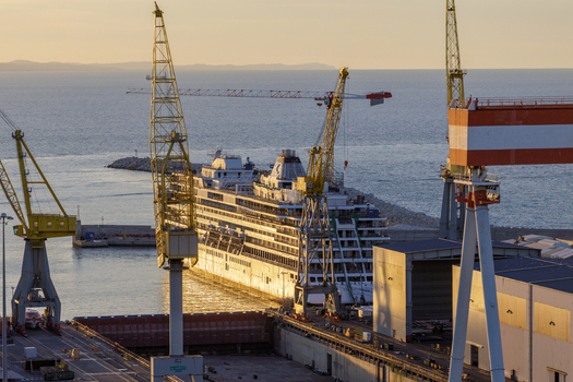 Aerial view of a cruise ship docked at the Ancona Port shipyard with large yellow cranes and industrial structures under golden hour light in Ancona Marche Italy. Aerial view of a cruise ship docked at the Ancona Port shipyard with large yellow cranes and industrial structures under golden hour light in Ancona Marche Italy.