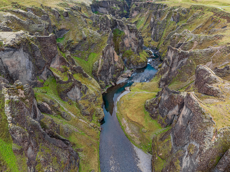 Aerial view of Fjadrargljufur canyon featuring steep rocky cliffs vibrant green mossy slopes and a winding river flowing through the dramatic landscape in Iceland. Aerial view of Fjadrargljufur canyon featuring steep rocky cliffs vibrant green mossy slopes and a winding river flowing through the dramatic landscape in Iceland.