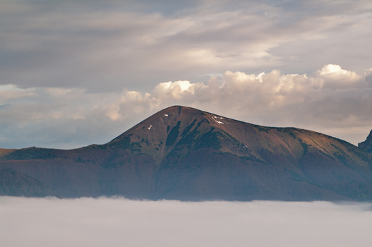 Aerial view of Stoh mountain in Mala Fatra rising above a thick layer of clouds with soft golden light on the peak in Turany Zilina Region Slovakia.