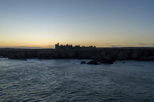 Aerial view of the silhouette of Slains Castle ruins on rugged cliffs overlooking the North Sea at sunset Cruden Bay Scotland United Kingdom. Aerial view of the silhouette of Slains Castle ruins on rugged cliffs overlooking the North Sea at sunset Cruden Bay Scotland United Kingdom.