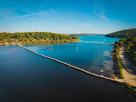 Aerial view of a footbridge stretching across the shimmering blue waters connecting verdant peninsulas under a clear sky Premantura Istria County Croatia.