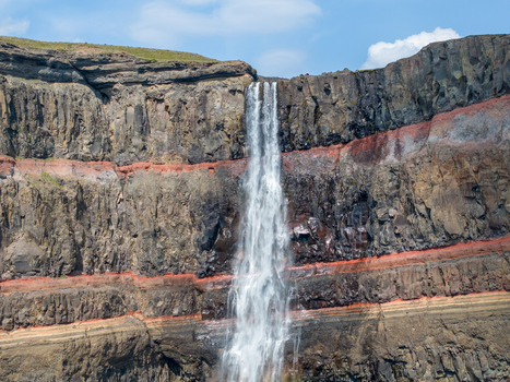 Aerial view of Hengifoss waterfall cascading down dramatic layered basalt and red clay cliffs in Iceland. Aerial view of Hengifoss waterfall cascading down dramatic layered basalt and red clay cliffs in Iceland.
