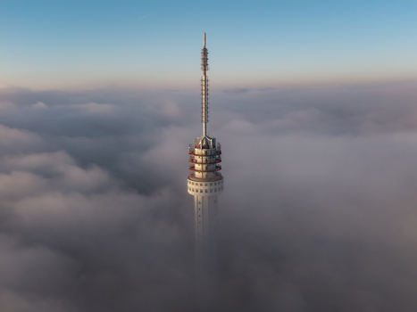 Aerial view of the telecommunications tower rising above a thick blanket of clouds under a clear blue sky in Roermond Limburg Netherlands.