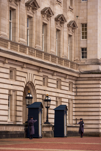 London United Kingdom 12 May 2025 View of Buckingham Palace with King s Guard soldiers standing at sentry boxes in front of the historic stone facade.