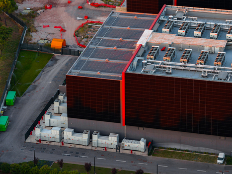 Aerial view of a modern datacenter with rooftop cooling units and ground level infrastructure surrounded by paved areas and greenery in Settecamini Lazio Italy.
