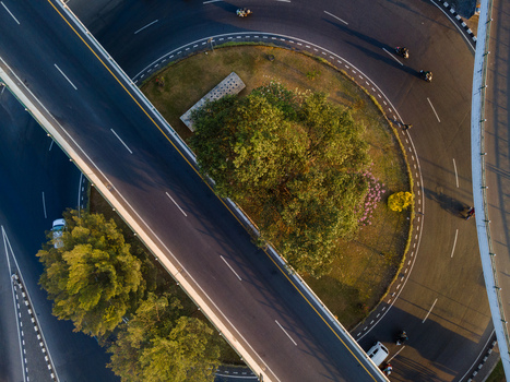 Aerial view of a highway interchange with curved roads lush green trees in the center and vehicles driving on the asphalt in Yogyakarta Special Region of Yogyakarta Indonesia. Aerial view of a highway interchange with curved roads lush green trees in the center and vehicles driving on the asphalt in Yogyakarta Special Region of Yogyakarta Indonesia.