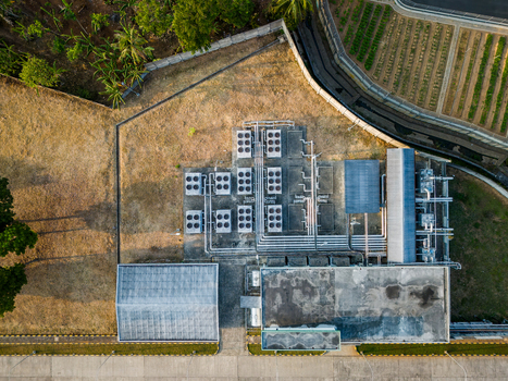 Aerial view of an industrial facility featuring multiple HVAC cooling units and piping systems situated near agricultural fields and trees in Semarang Regency Central Java Indonesia. Aerial view of an industrial facility featuring multiple HVAC cooling units and piping systems situated near agricultural fields and trees in Semarang Regency Central Java Indonesia.