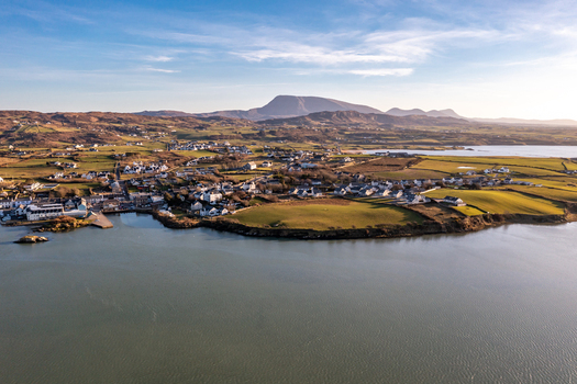 Aerial view of Dunfanaghy village nestled along the coastline with green fields stone walls and rolling hills under a clear blue sky in Dunfanaghy County Donegal Ireland. Aerial view of Dunfanaghy village nestled along the coastline with green fields stone walls and rolling hills under a clear blue sky in Dunfanaghy County Donegal Ireland.