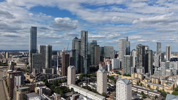 London United Kingdom 16 June 2026 Aerial view of the Canary Wharf skyline featuring modern skyscrapers and residential buildings under a blue sky with scattered clouds.