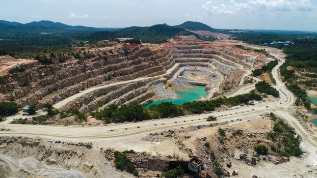 Aerial view of a large open pit gravel mine with terraced walls turquoise water at the bottom and heavy machinery on the surrounding dirt roads in Karimun Kepulauan Riau Indonesia.