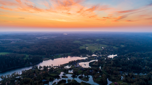 Aerial view of a serene lake surrounded by dense forests under a vibrant sunset sky in Latvia. Aerial view of a serene lake surrounded by dense forests under a vibrant sunset sky in Latvia.