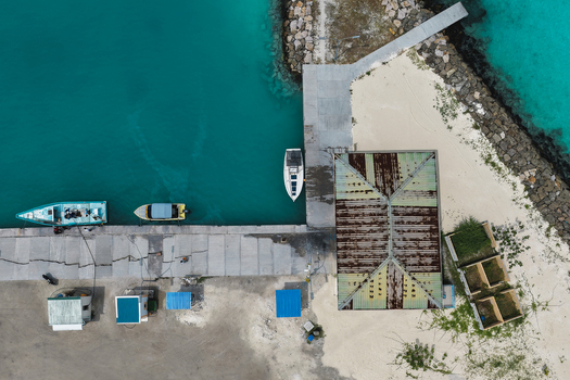Aerial view of boats docked at a concrete pier next to turquoise waters and a weathered building in Hanimaadhoo Haa Dhaalu Atoll Maldives.