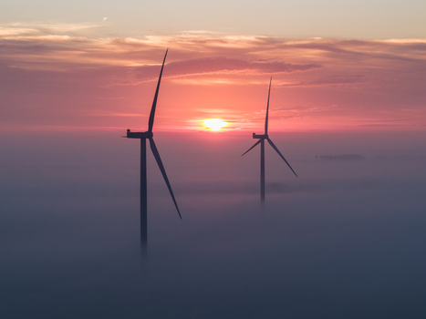 Aerial view of two wind turbines rising above a thick layer of morning fog during a vibrant orange sunrise Vrouwenpolder Zeeland Netherlands.
