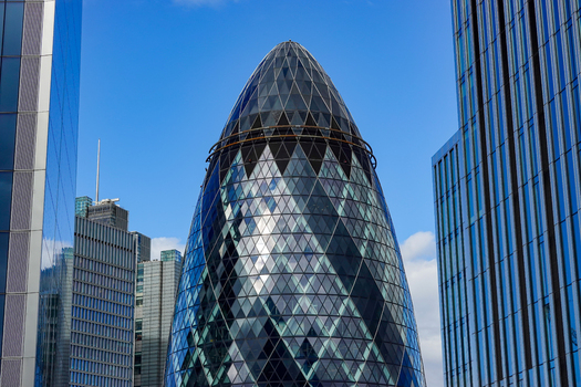 View of 30 St Mary Axe also known as The Gherkin featuring its iconic glass and steel facade rising against a clear blue sky in the financial district of London England United Kingdom.
