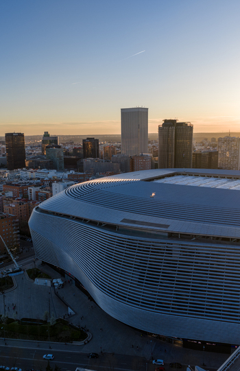 Aerial view of Santiago Bernabeu stadium featuring its modern metallic facade and the surrounding Madrid city skyline during golden hour in Madrid Community of Madrid Spain. Aerial view of Santiago Bernabeu stadium featuring its modern metallic facade and the surrounding Madrid city skyline during golden hour in Madrid Community of Madrid Spain.