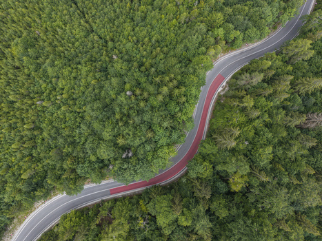 Aerial view of a winding road through a dense green forest with a distinct red lane section in Vernar Presovsky kraj Slovakia. Aerial view of a winding road through a dense green forest with a distinct red lane section in Vernar Presovsky kraj Slovakia.