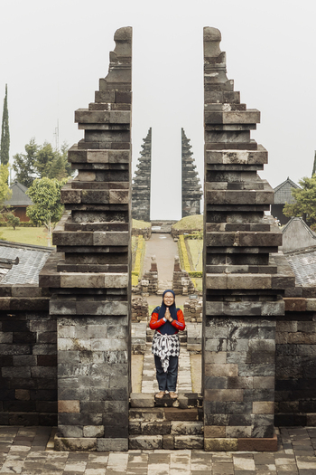 View of a woman standing between the stone split gates of Cetho Temple with tiered architecture and misty mountain atmosphere Kecamatan Jenawi Jawa Tengah Indonesia. View of a woman standing between the stone split gates of Cetho Temple with tiered architecture and misty mountain atmosphere Kecamatan Jenawi Jawa Tengah Indonesia.