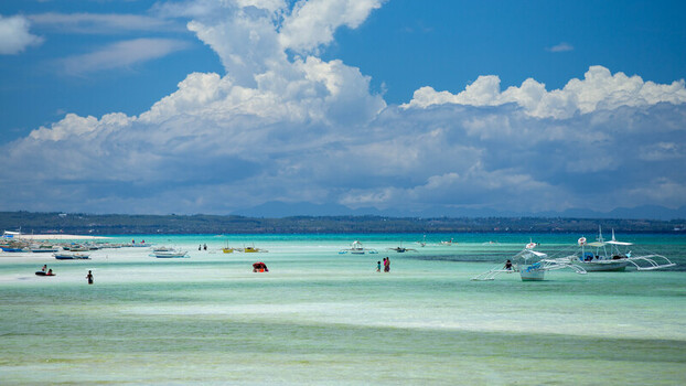View of Bantayan Island with traditional outrigger boats anchored in shallow turquoise water and people wading under a bright blue sky in Cebu Central Visayas Philippines. View of Bantayan Island with traditional outrigger boats anchored in shallow turquoise water and people wading under a bright blue sky in Cebu Central Visayas Philippines.