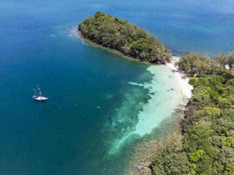 Aerial view of the lush tropical coastline with turquoise waters a white sandy beach and a boat anchored in the bay in Guanaja Bay Islands Department Honduras. Aerial view of the lush tropical coastline with turquoise waters a white sandy beach and a boat anchored in the bay in Guanaja Bay Islands Department Honduras.