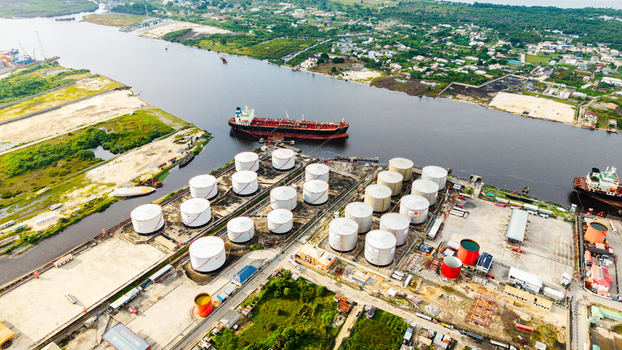 Aerial view of the industrial oil storage facility in Satellite Town featuring large white storage tanks a cargo ship in the river and port infrastructure in Lagos Lagos Nigeria.