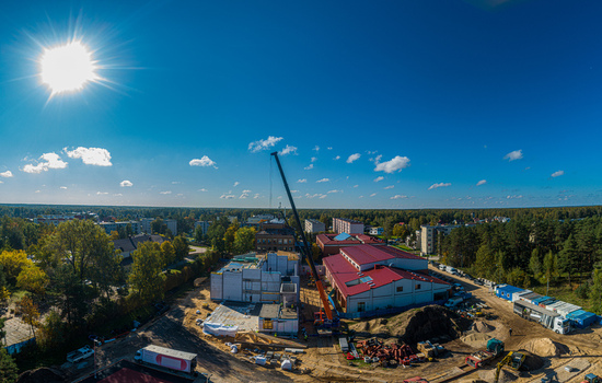 Aerial view of a construction site featuring a tall crane modern buildings with red roofs and surrounding forest under a bright sunny sky in Latvia. Aerial view of a construction site featuring a tall crane modern buildings with red roofs and surrounding forest under a bright sunny sky in Latvia.