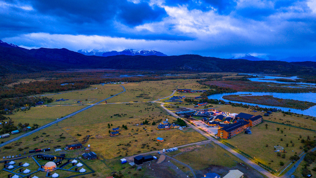 Aerial view of Rio Serrano Hotel Spa with illuminated buildings at twilight a winding river and snow capped mountains in Torres de Paine Magallanes Chile. Aerial view of Rio Serrano Hotel Spa with illuminated buildings at twilight a winding river and snow capped mountains in Torres de Paine Magallanes Chile.