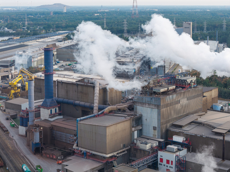 Aerial view of the industrial steel manufacturing complex at Genk Zuid Rechteroever with large chimneys emitting steam complex piping systems and surrounding greenery in Genk Vlaanderen Belgium. Aerial view of the industrial steel manufacturing complex at Genk Zuid Rechteroever with large chimneys emitting steam complex piping systems and surrounding greenery in Genk Vlaanderen Belgium.