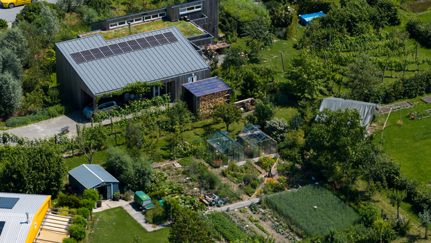 Aerial view of Ecodorp Bolderburen featuring modern sustainable houses with solar panels and green roofs surrounded by lush vegetable gardens and greenhouses in Almere Flevoland Netherlands. Aerial view of Ecodorp Bolderburen featuring modern sustainable houses with solar panels and green roofs surrounded by lush vegetable gardens and greenhouses in Almere Flevoland Netherlands.