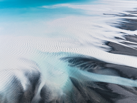 Aerial view of glacial rivers carving through the stark contrasting landscape with icy blues meeting dark earth where birds fly over Lake Tekapo Canterbury Region New Zealand. Aerial view of glacial rivers carving through the stark contrasting landscape with icy blues meeting dark earth where birds fly over Lake Tekapo Canterbury Region New Zealand.