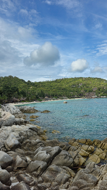 View of the rocky coastline and turquoise waters of Ko Tao surrounded by lush green hills under a blue sky in Ko Tao Surat Thani Thailand.