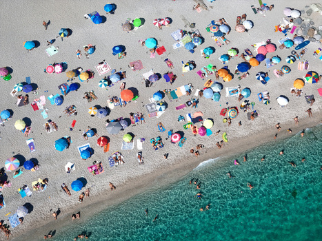 Aerial view of a crowded public beach with colorful umbrellas and people swimming in the turquoise water of the Mediterranean Sea in Bergeggi Liguria Italy.