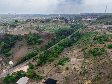 Aerial view of a winding road cutting through a dry undulating landscape with scattered green foliage and distant buildings under an overcast sky Ohafia Abia Nigeria. Aerial view of a winding road cutting through a dry undulating landscape with scattered green foliage and distant buildings under an overcast sky Ohafia Abia Nigeria.