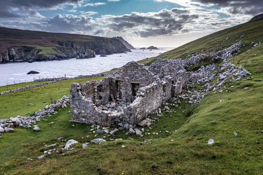 Aerial view of the ruins of An Port stone cottage situated on a grassy coastal slope overlooking the rugged cliffs and Atlantic Ocean in Ardara County Donegal Ireland.