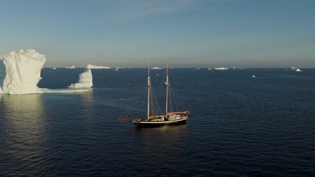 Aerial view of a sailboat near an arch iceberg in Greenland. Aerial view of a sailboat near an arch iceberg in Greenland.