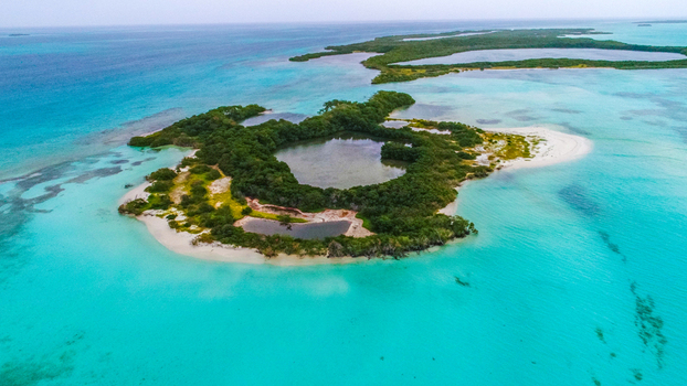 Aerial view of Los Roques archipelago featuring a lush green island with a central lagoon surrounded by turquoise Caribbean waters in Los Roques Dependencias Federales Venezuela. Aerial view of Los Roques archipelago featuring a lush green island with a central lagoon surrounded by turquoise Caribbean waters in Los Roques Dependencias Federales Venezuela.