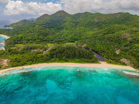 Aerial view of turquoise waters meet the sandy beach and lush green forests of Mahe Island a tropical paradise under a cloudy sky Police Bay Mahe Island Seychelles. Aerial view of turquoise waters meet the sandy beach and lush green forests of Mahe Island a tropical paradise under a cloudy sky Police Bay Mahe Island Seychelles.