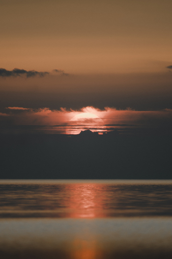 View of the sunset over the sea with orange clouds and light reflecting on the calm water at Vormsi Laane County Estonia. View of the sunset over the sea with orange clouds and light reflecting on the calm water at Vormsi Laane County Estonia.