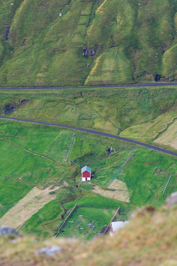 View of a red house with a green roof situated in a lush green valley in the Faroe Islands. View of a red house with a green roof situated in a lush green valley in the Faroe Islands.