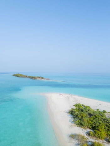 Aerial view of turquoise waters swirling around a pristine island creating a mesmerizing contrast against the white sandy beach Dhidhdhoo Thiladhunmathi Atoll Maldives.
