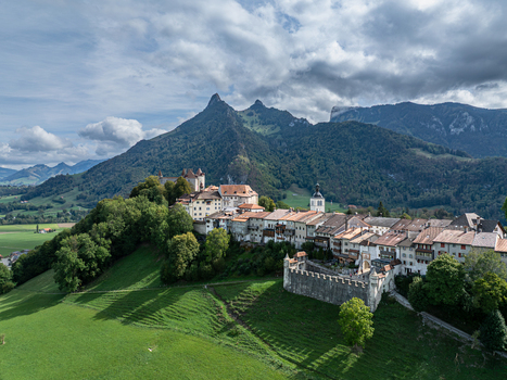 Aerial view of Chateau de Gruyeres perched on a hill above the historic town surrounded by green meadows forests and Prealps peaks under a cloudy sky Gruyeres Fribourg Switzerland. Aerial view of Chateau de Gruyeres perched on a hill above the historic town surrounded by green meadows forests and Prealps peaks under a cloudy sky Gruyeres Fribourg Switzerland.