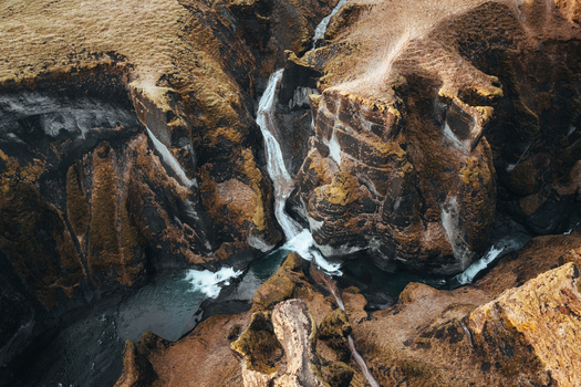 Aerial view of the river carving its way through the rugged golden brown canyon walls creating a dramatic landscape of water and stone Fjadrargljufur Iceland. Aerial view of the river carving its way through the rugged golden brown canyon walls creating a dramatic landscape of water and stone Fjadrargljufur Iceland.
