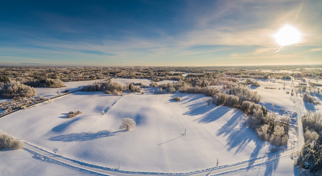 Aerial view of a snow covered landscape with frost covered trees open fields and a winding road under a bright sun in Latvia. Aerial view of a snow covered landscape with frost covered trees open fields and a winding road under a bright sun in Latvia.