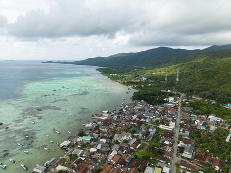 Aerial view of the coastal village nestled between the turquoise sea and verdant hills under a cloudy sky Karimunjawa Central Java Indonesia. Aerial view of the coastal village nestled between the turquoise sea and verdant hills under a cloudy sky Karimunjawa Central Java Indonesia.