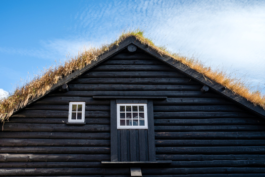 View of a traditional black wooden house with a grass covered turf roof under a clear blue sky in the Faroe Islands. View of a traditional black wooden house with a grass covered turf roof under a clear blue sky in the Faroe Islands.