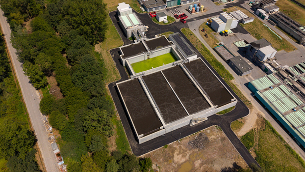 Aerial view of a wastewater treatment plant featuring large sedimentation tanks with green water industrial infrastructure and surrounding lush green trees in Milan Lombardy Italy. Aerial view of a wastewater treatment plant featuring large sedimentation tanks with green water industrial infrastructure and surrounding lush green trees in Milan Lombardy Italy.